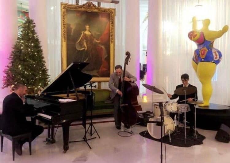 Un trio de jazz performant dans une salle ornée d'œuvres d'art, avec un pianiste, un contrebassiste et un batteur offrant une ambiance élégante.