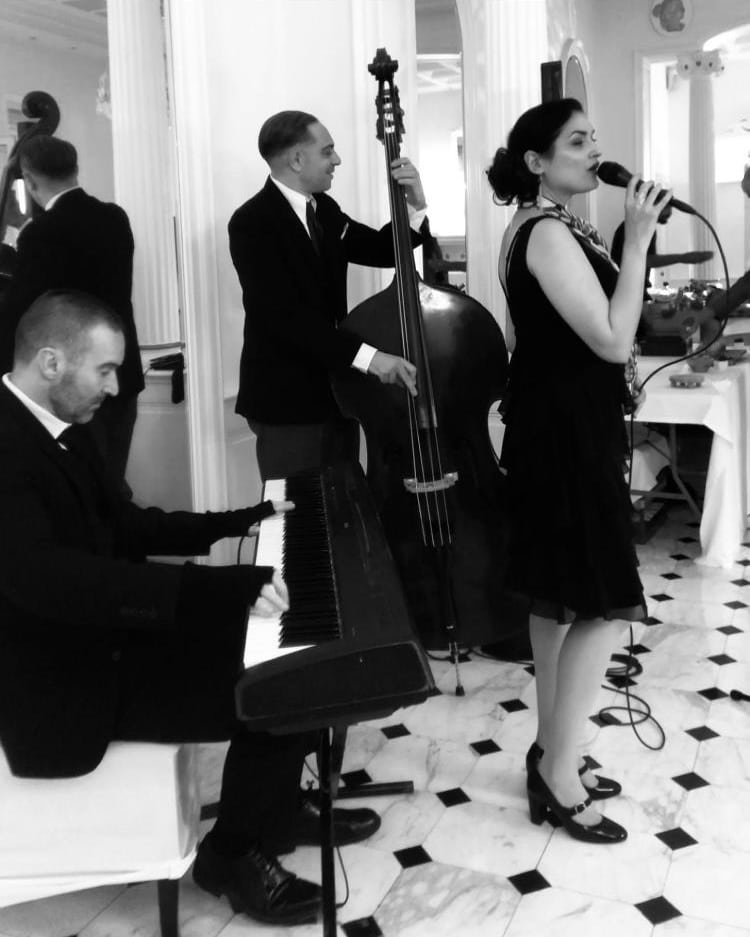 Un orchestre de jazz en pleine performance avec une chanteuse, un contrebassiste et un pianiste lors d'un événement élégant, créant une ambiance musicale captivante.